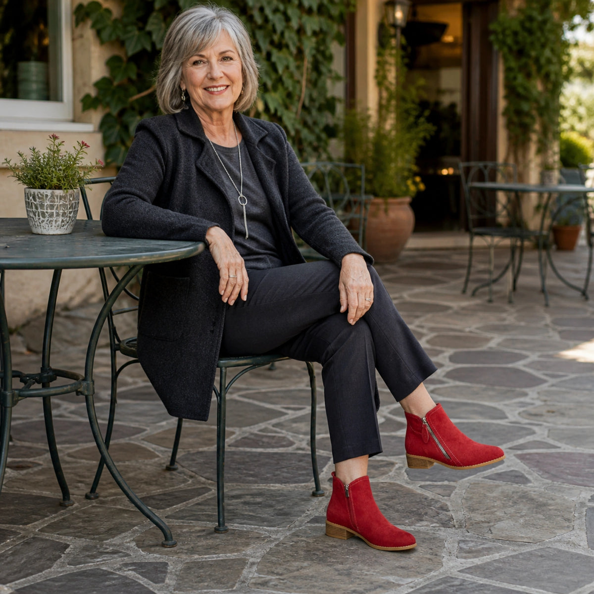 Mature woman wearing crimson suede zip ankle boots in an outdoor courtyard — view 11