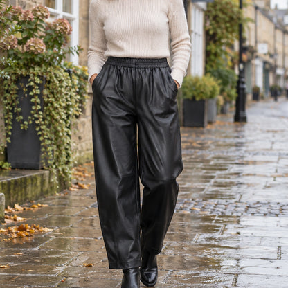 leather trousers — Front view of the full Black trousers worn by an adult model in a cool UK autumn street setting