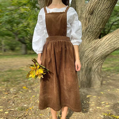 Brown corduroy midi jumper dress with square neck and button details, worn in a natural setting — view 9 — view 14