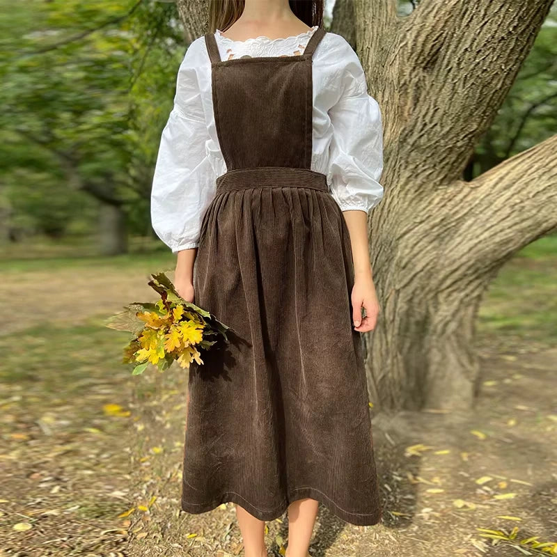 Woman wearing a brown corduroy midi jumper dress with button details and square neck, holding autumn leaves — view — view 15