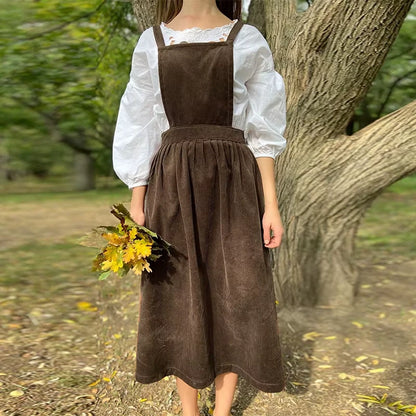 Woman wearing a brown corduroy midi jumper dress with button details and square neck, holding autumn leaves — view — view 15