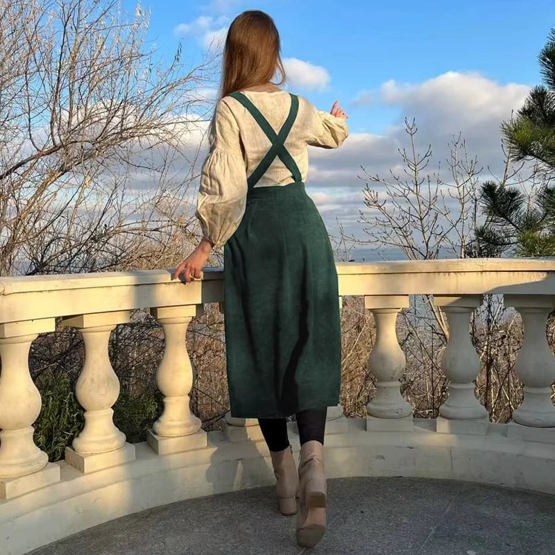 Woman wearing a green corduroy midi jumper dress with button details, standing on balcony — view 2 — view 7