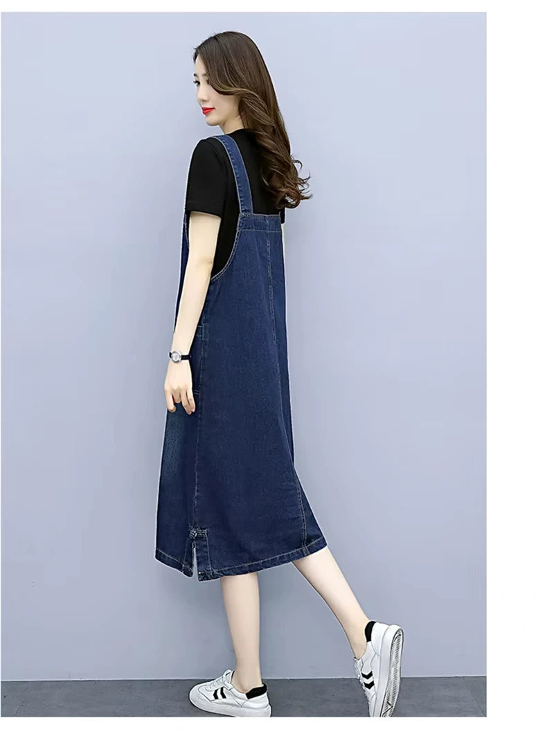 Woman wearing a loose fit denim knee length midi jumper dress, side view — 16 — view 17