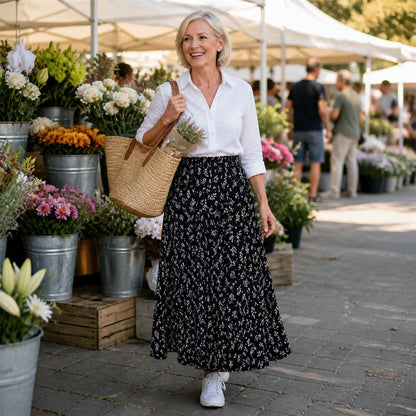 pleated skirt — Woman in her sixties wearing a black floral skirt at an outdoor flower market — view 10