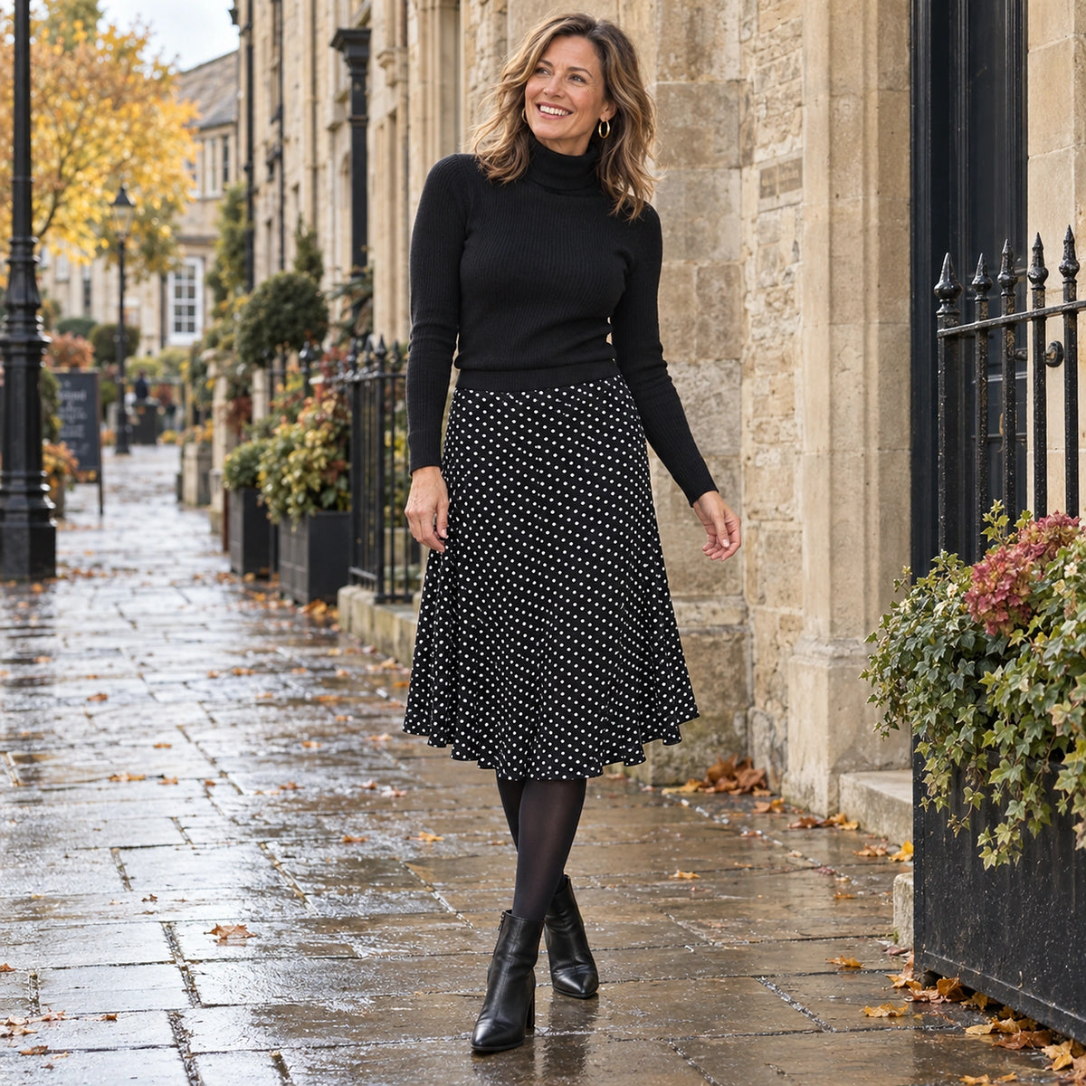 Happy adult model wearing the full Black Luna Polka Dot Low Rise Midi Pleated Skirt in a cool UK autumn setting — view 2