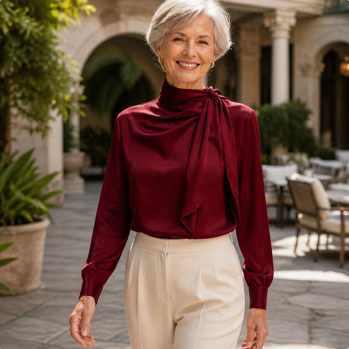Woman in her sixties wearing a burgundy scarf neck satin blouse heritage courtyard — view 8