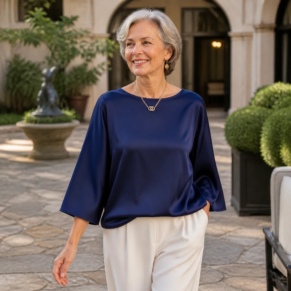 Woman in her sixties wearing a navy loose satin blouse an art hotel courtyard — view 10