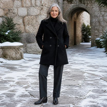 winter coat — Mature woman wearing black shearling trim coat in a snowy stone courtyard — view 8